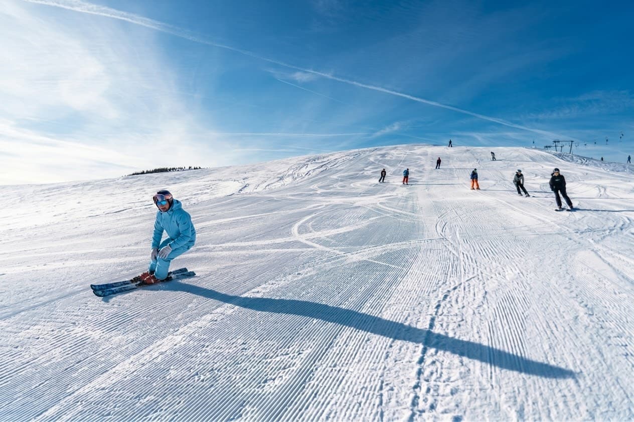 Un moniteur en tenue bleu ciel sur la piste, skieurs en arrière-plan