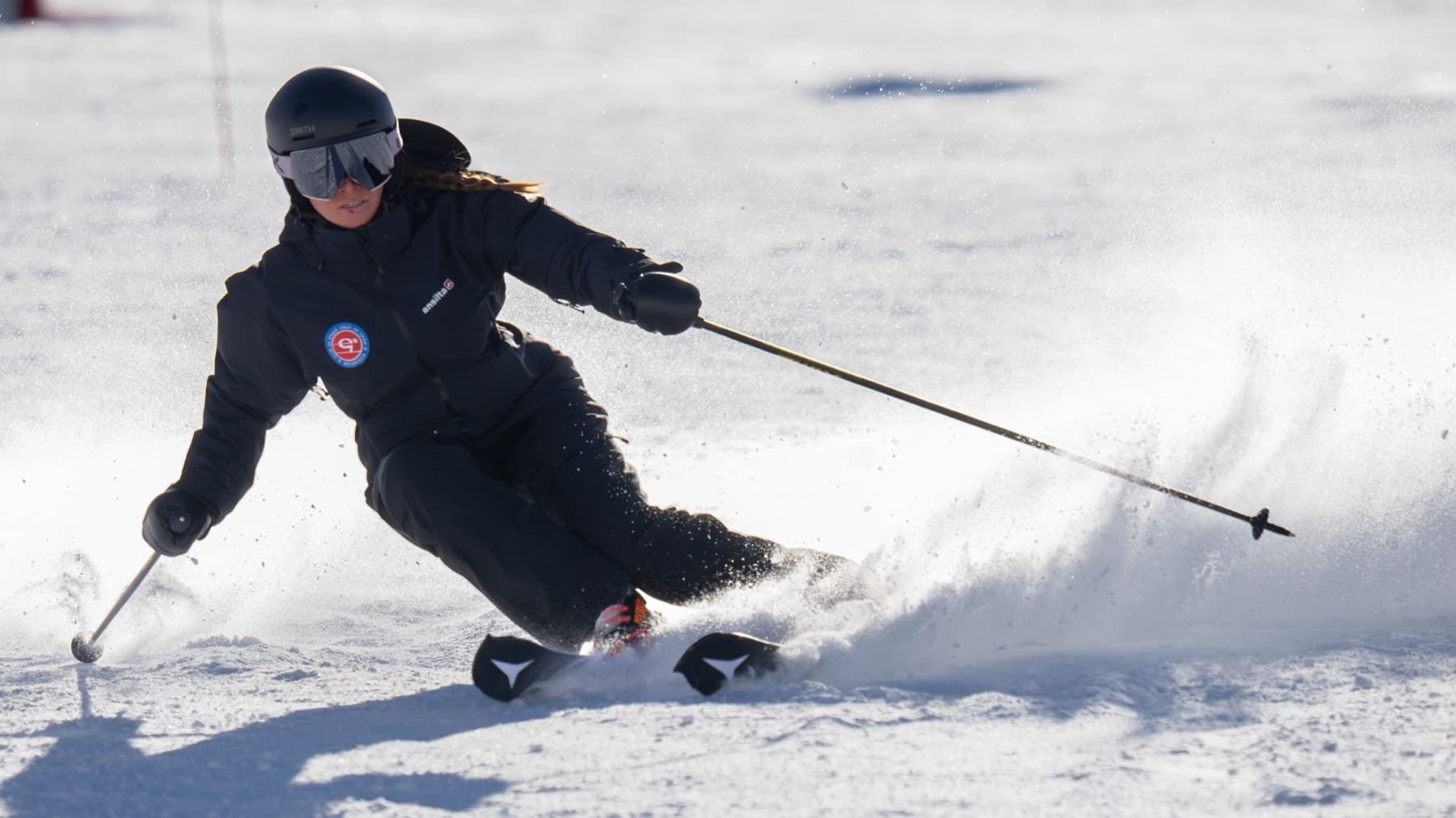 Une monitrice en tenue noire en pleine courbe sur la piste