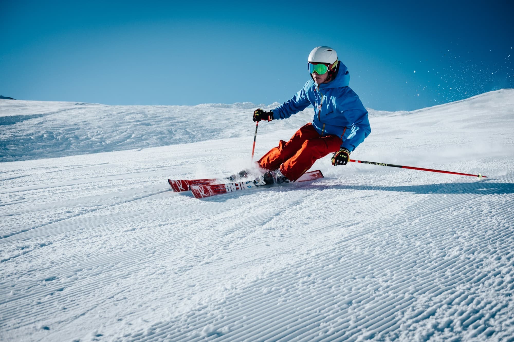 Un skieur en veste bleue à pleine vitesse sur une piste damée
